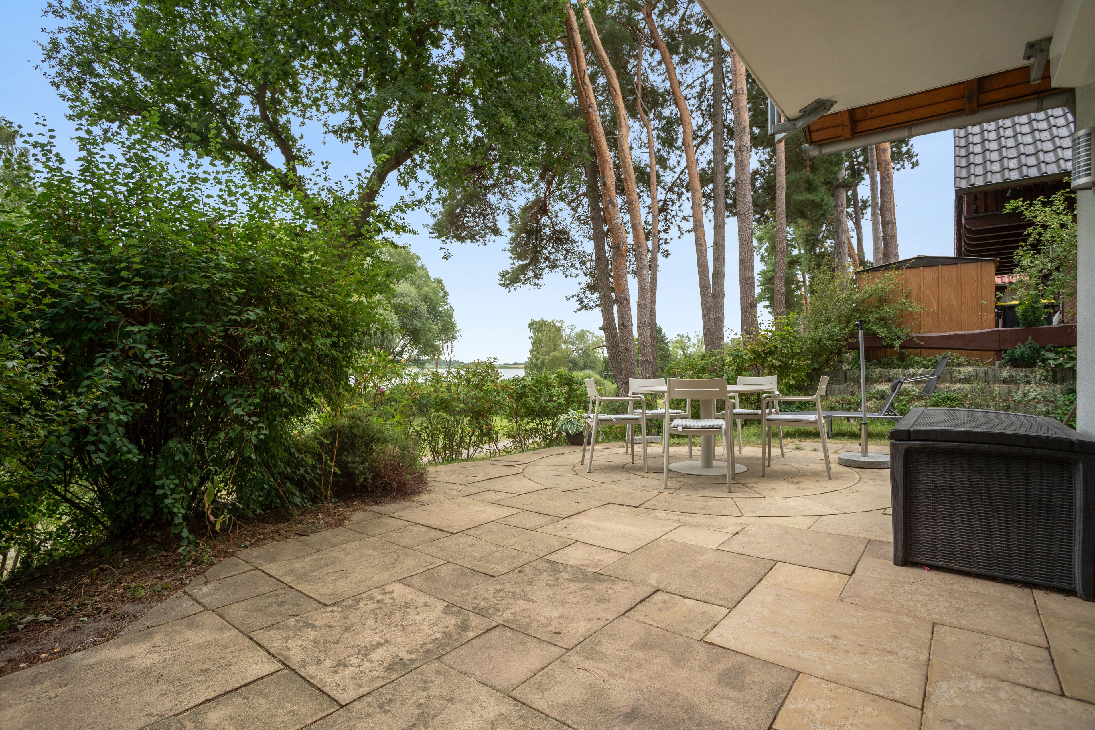 Un espace patio doté d’un sol en pierre, de mobilier d’extérieur et de grands arbres.