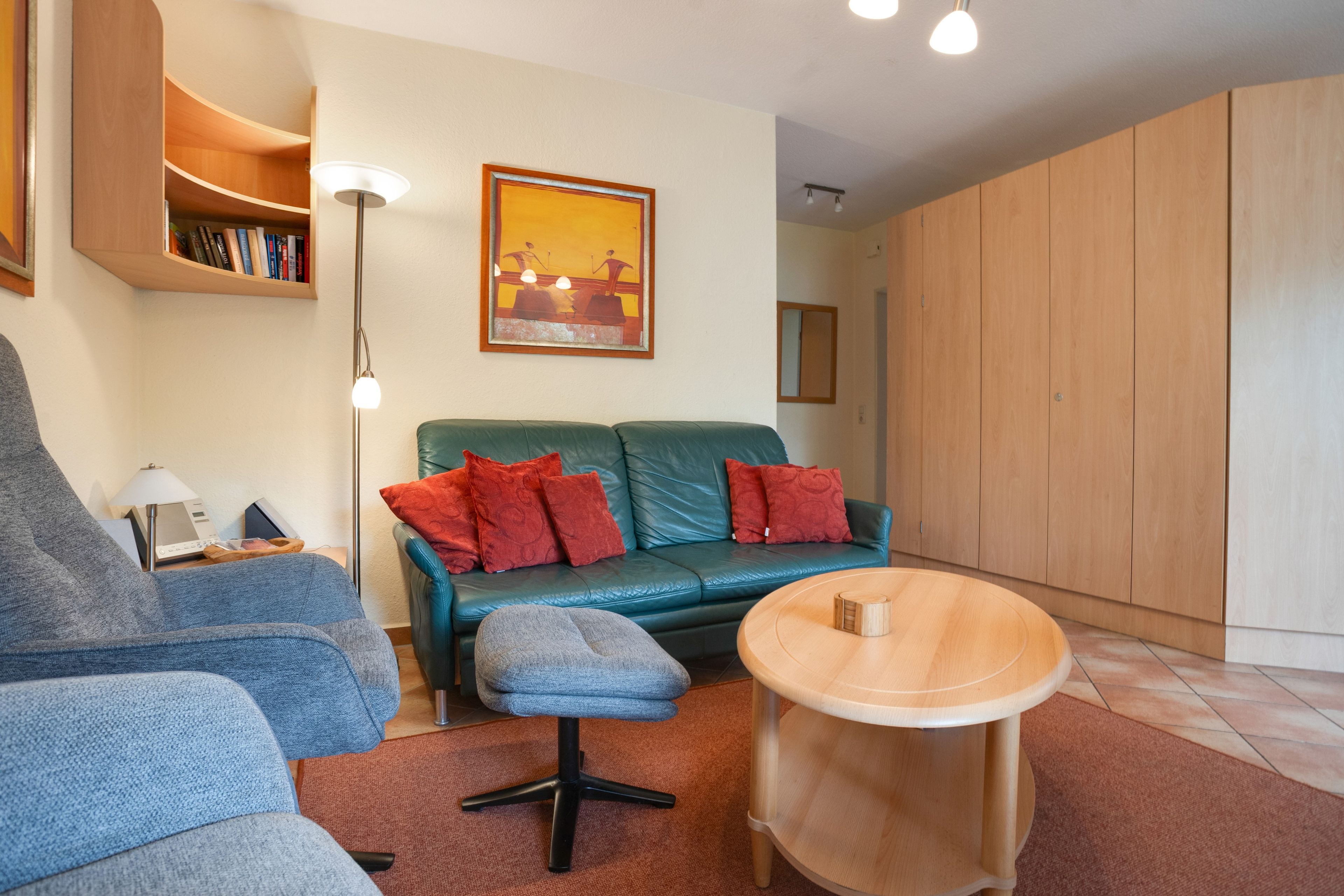 Un salon moderne avec un canapé bleu, des coussins rouges, une table basse en bois et une bibliothèque.