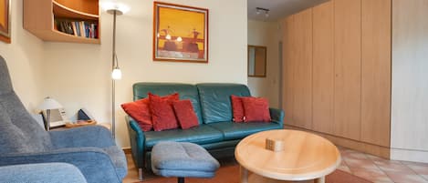 Un salon moderne avec un canapé bleu, des coussins rouges, une table basse en bois et une bibliothèque.