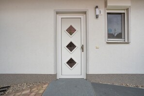 Eine weiße Tür mit drei rautenförmigen Fenstern, einem kleinen Fenster darüber und einem Fenster mit Blick auf Bäume.
