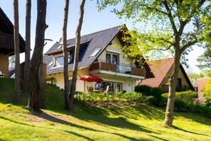 Ein zweistöckiges Haus mit geneigtem Dach und einem Balkon, mit einem roten Sonnenschirm.