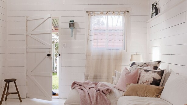A room with a bed, a hanging light fixture, a window with curtains, and a door leading outside.