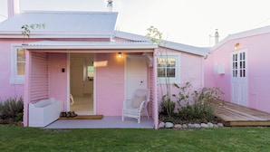 A pink house with a porch, a white chair, and a small garden.