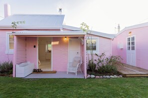 Een roze huis met een veranda, een witte stoel en een kleine tuin.
