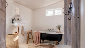 A bathroom with a white sink, a black bathtub, a wooden stool, a woven basket, and a fur rug.