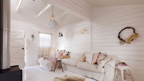 A room with white wooden walls, a white sofa, a small stool, and a fur rug.