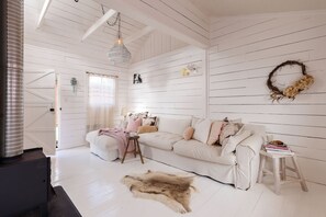 Een kamer met witte houten wanden, een witte bank, een klein krukje en een bont tapijt.