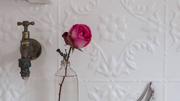 A bathroom with a white sink, a rose in a glass jar, and a towel hanging on a rack.