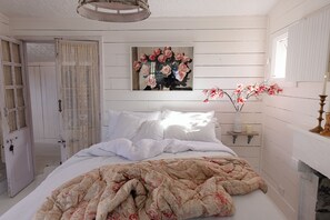 Een slaapkamer met een bed, een schilderij, een vaas met bloemen en een deur.