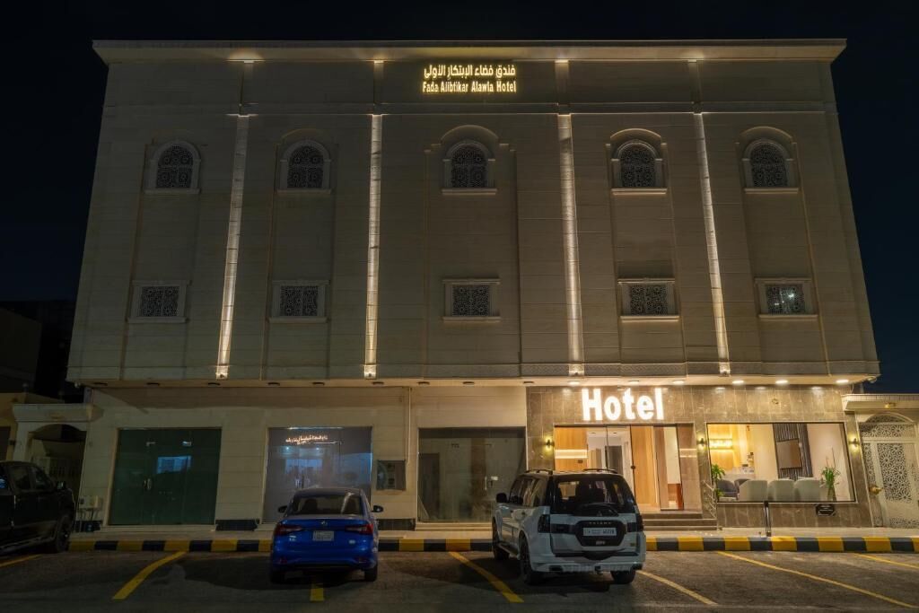 Edifício de hotel com placa indicando ser o Fada Alibitar Alamia Hotel. Dois carros estacionados em frente.