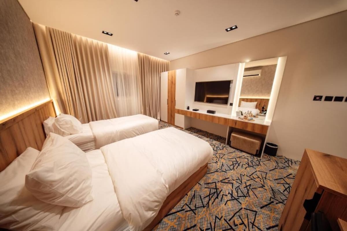 Quarto de hotel com duas camas, uma escrivaninha, um espelho e uma televisão.