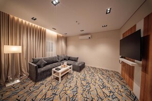 Una habitación de hotel moderna con un sofá seccional, una mesa de centro, un televisor de pantalla plana y una alfombra estampada.