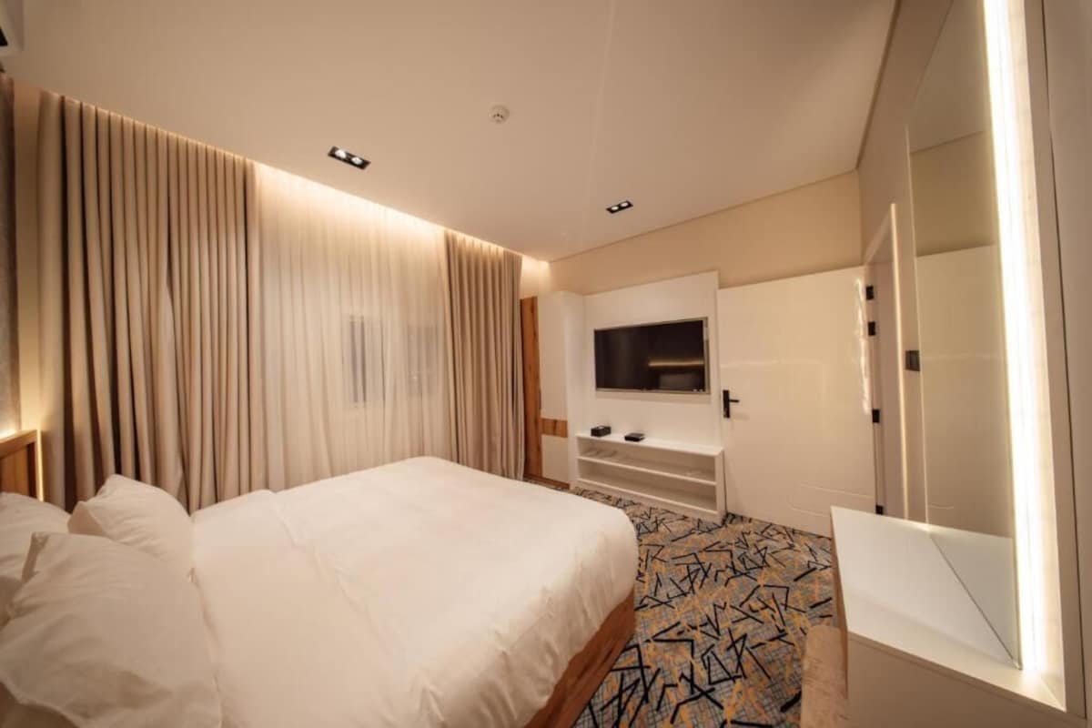 Quarto de hotel com cama, cortinas, televisão e minibar.