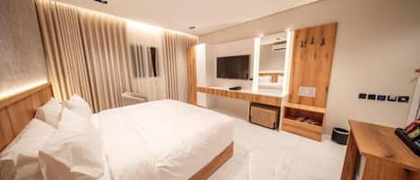 Een moderne hotelkamer met een groot bed, een houten bureau, een televisie en een spiegel.