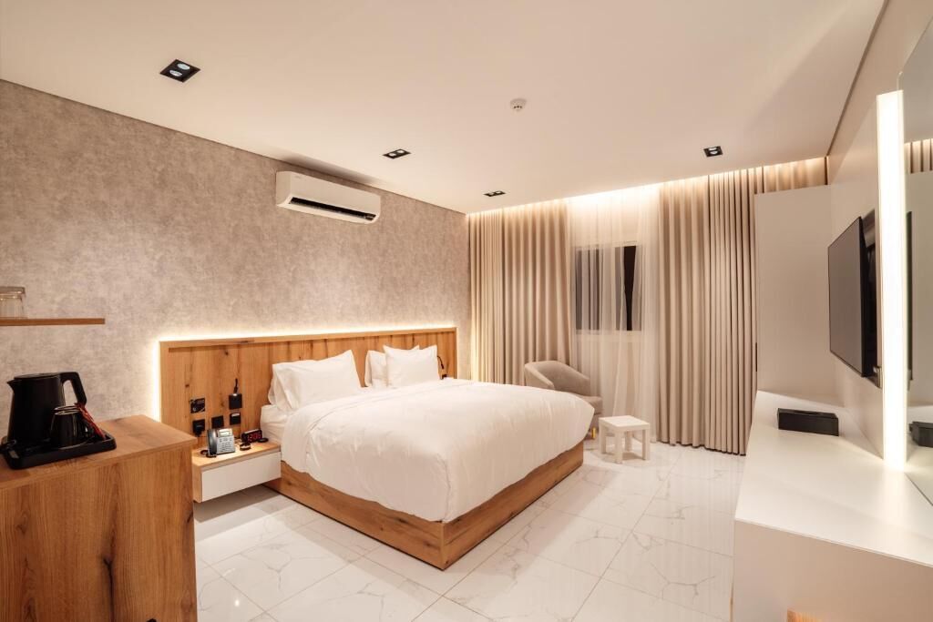 Quarto de hotel moderno com uma cama grande, mesas de cabeceira, TV e cafeteira.