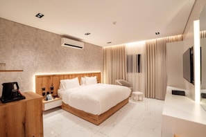 Quarto de hotel moderno com uma cama grande, mesas de cabeceira, TV e cafeteira.