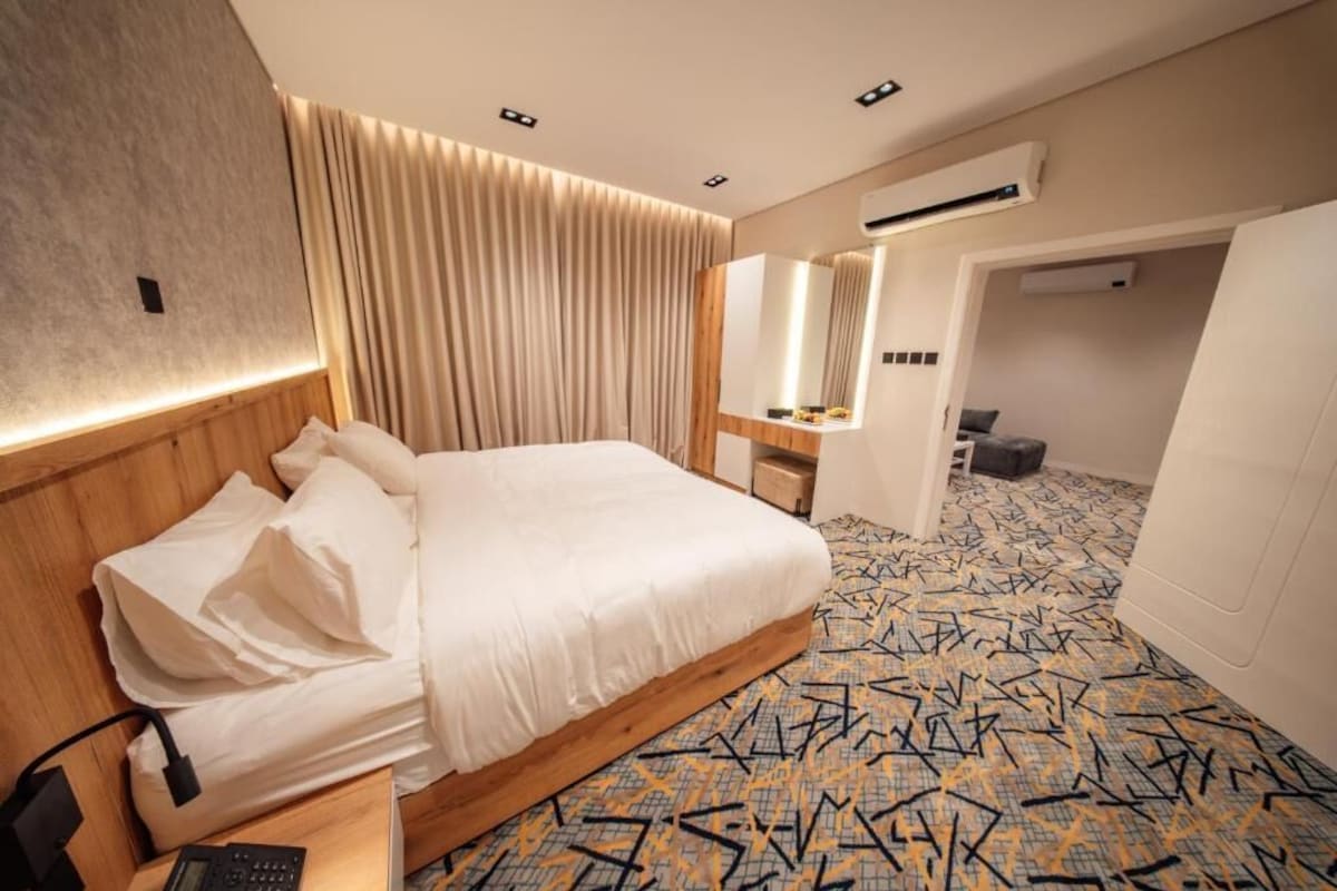 Quarto de hotel com cama, mesa de cabeceira, espelho, ar condicionado e piso estampado.