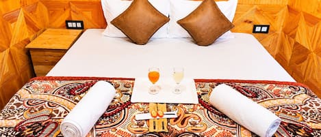 Una cama bien hecha con una colcha estampada, dos almohadas y una bandeja con vasos y una botella.