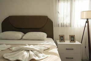 A neatly made bed with pillows, a bedside table with two framed pictures, and a floor lamp. - Beach Suite L Penthouse İcmeler (Muğla)
