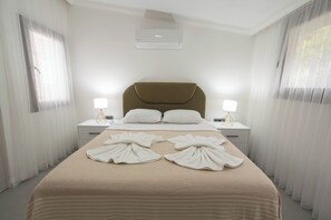 A hotel room with a large bed, two bedside tables with lamps, a headboard, and a ceiling air conditioner. - Beach Suite L Penthouse İcmeler (Muğla)