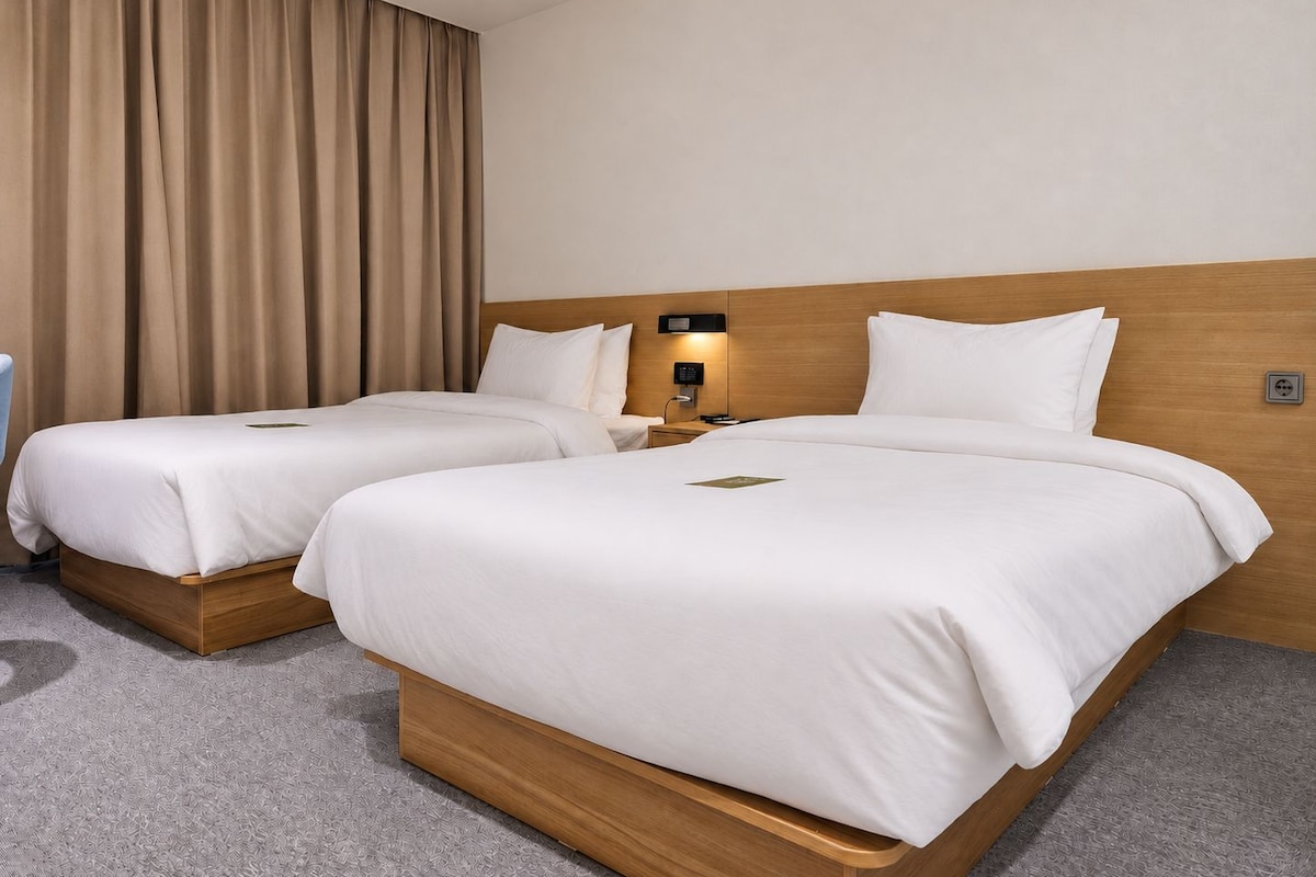 Een hotelkamer met twee bedden, een houten hoofdeinde, een nachtkastje, een lamp en een gordijn.