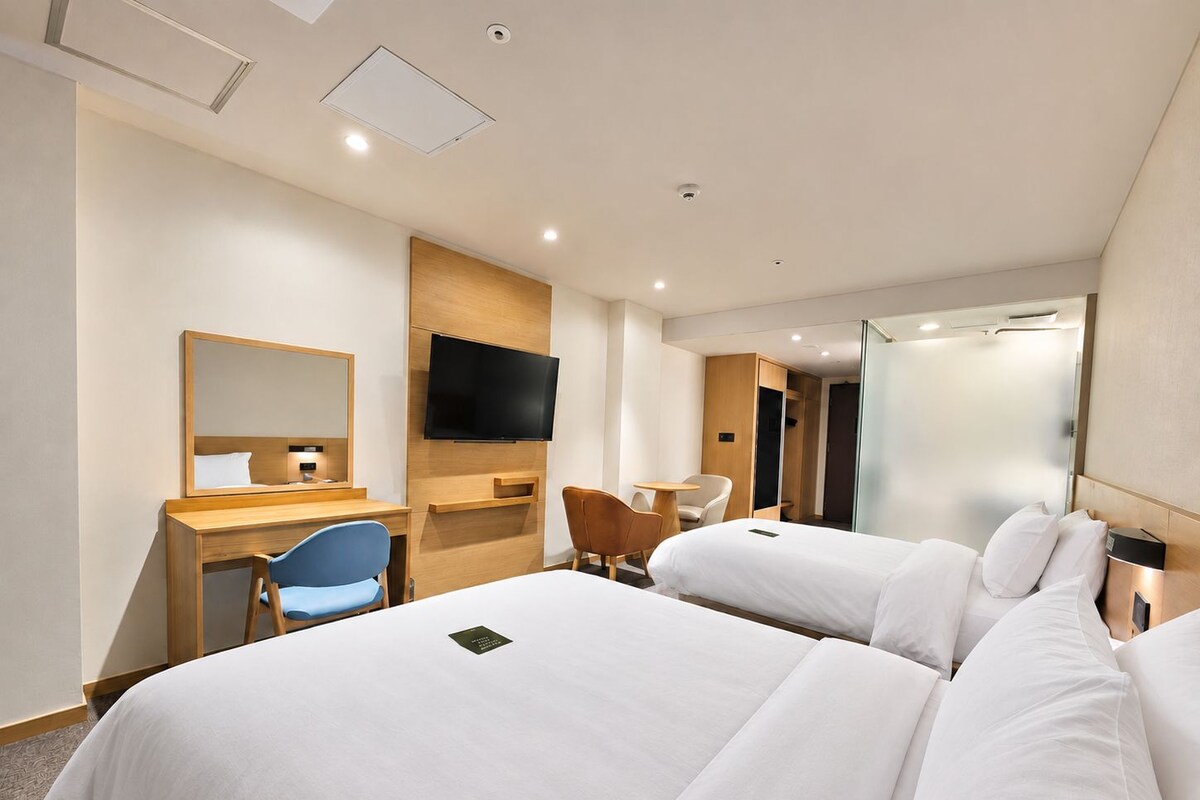 Een hotelkamer met twee bedden, een bureau, een stoel, een televisie en een kledingkast.