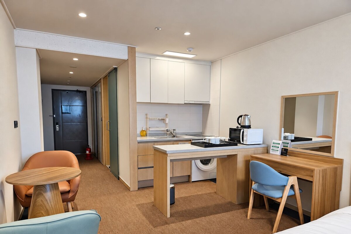 Een kleine hotelkamer met een kitchenette, een bed, een bureau en een stoel.