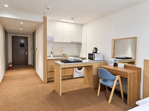 Een kleine hotelkamer met een kitchenette, een wasmachine, een magnetron, een koffiezetapparaat en een bureau met een stoel.