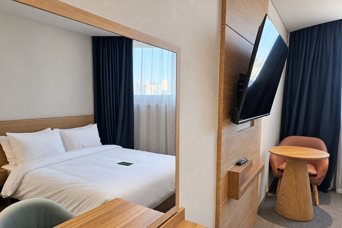Een hotelkamer met een bed, een aan de muur bevestigde televisie, een tafeltje en een stoel.