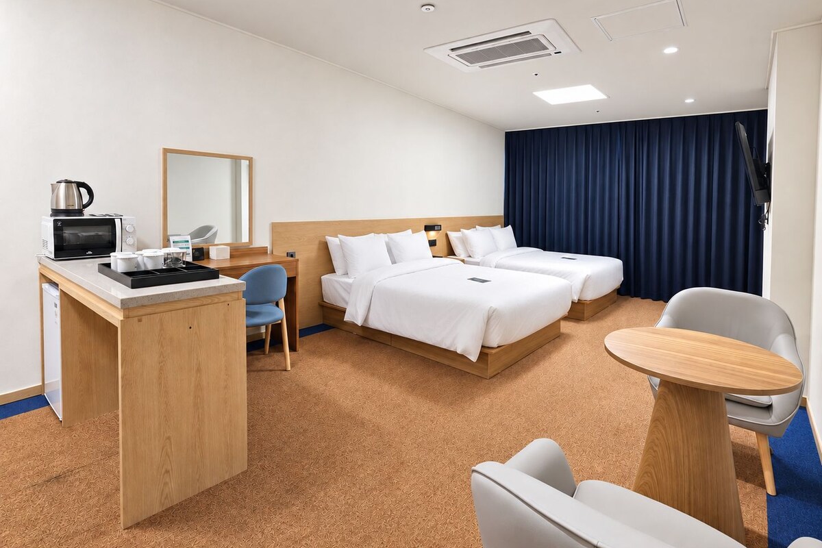 Een hotelkamer met een bureau, magnetron, twee bedden, een stoel en een televisie.