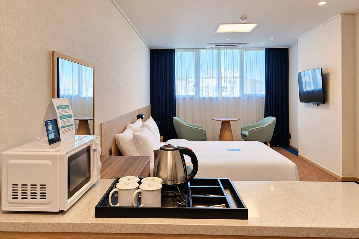 Een hotelkamer met een bed, een bureau met een magnetron, een dienblad met mokken, een koffiezetapparaat en een televisie aan de muur.