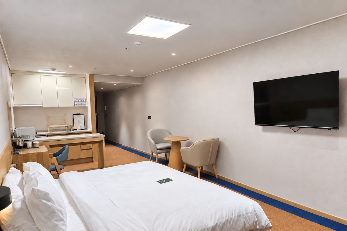 Een hotelkamer met een bed, een bureau met stoel, een kleine tafel met stoel, een flatscreen televisie aan de muur en een badkamer met douche en toilet.