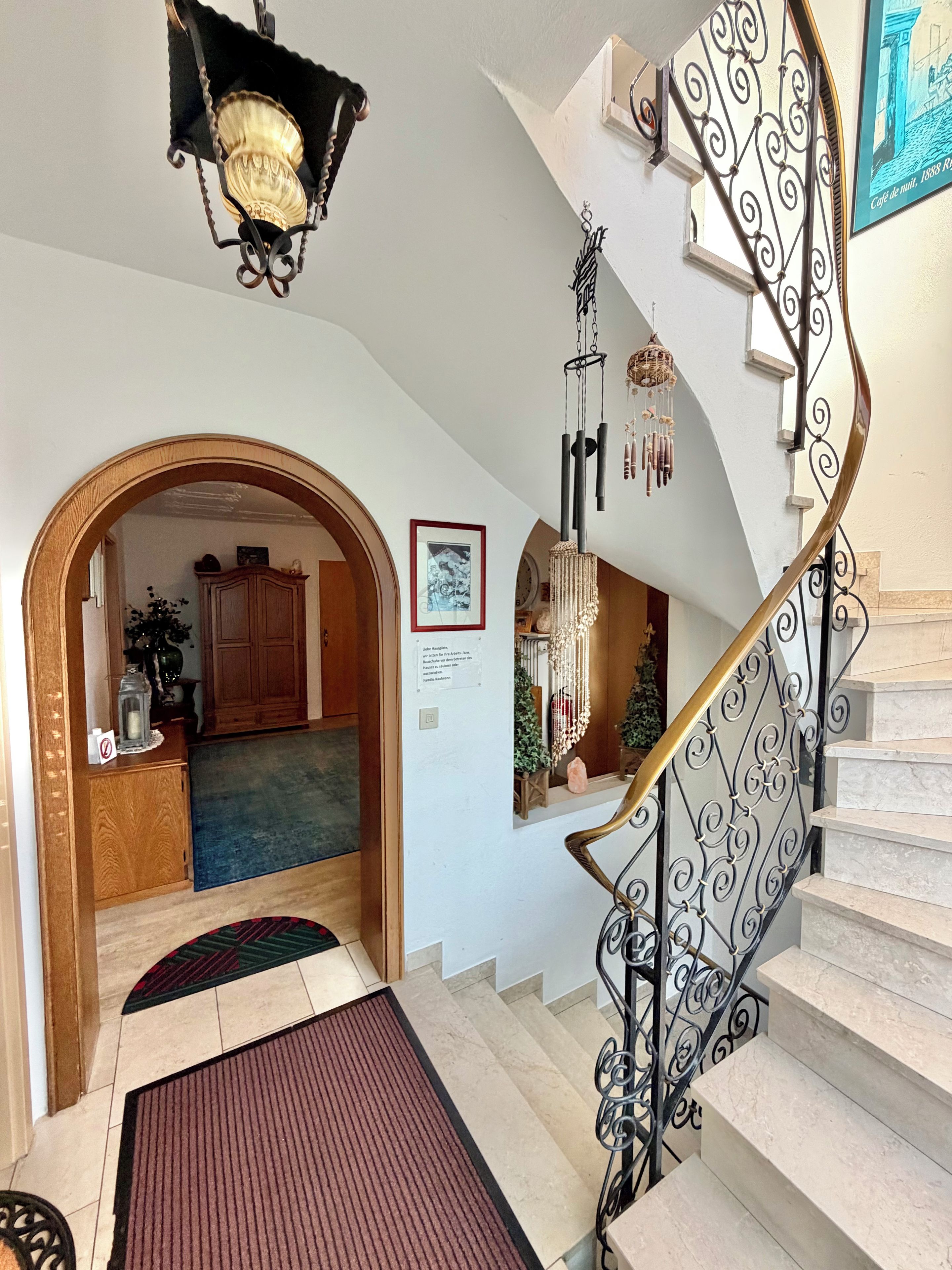 Eine Treppe mit aufwendiger Metallreling, einer Kristallleuchtre und einem gerahmten Bild an der Wand.