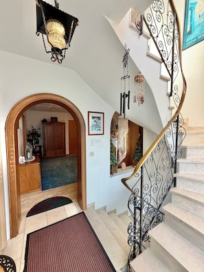 Una escalera con barandillas metálicas decorativas, un candelabro y un cuadro en la pared.