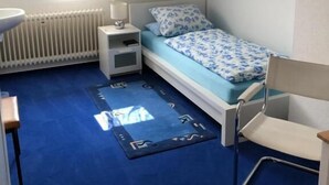 Ein Schlafzimmer mit Bett, Stuhl, Schreibtisch, Heizkörper und einem Fenster mit Vorhängen.
