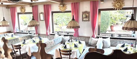 Un restaurante con mobiliario de madera, cortinas rosas y ventanas amplias.