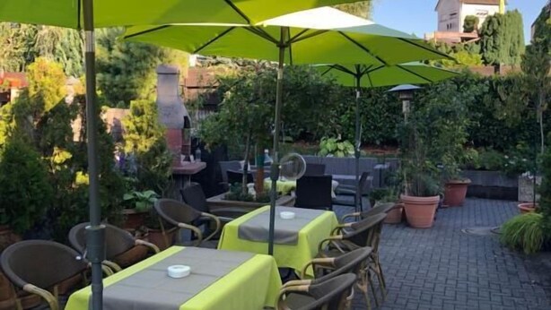 Terrasse mit Tischen, Stühlen, Sonnenschirmen und Pflanzkübeln.