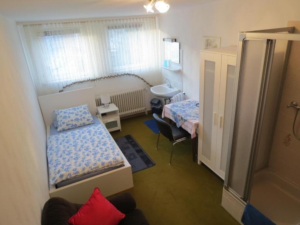 A compact room with a bed, a small desk, a chair, a radiator, and a wardrobe.