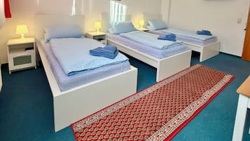 Habitación de hotel con dos camas, un televisor, un tapete rojo estampado y un ventilador de techo.