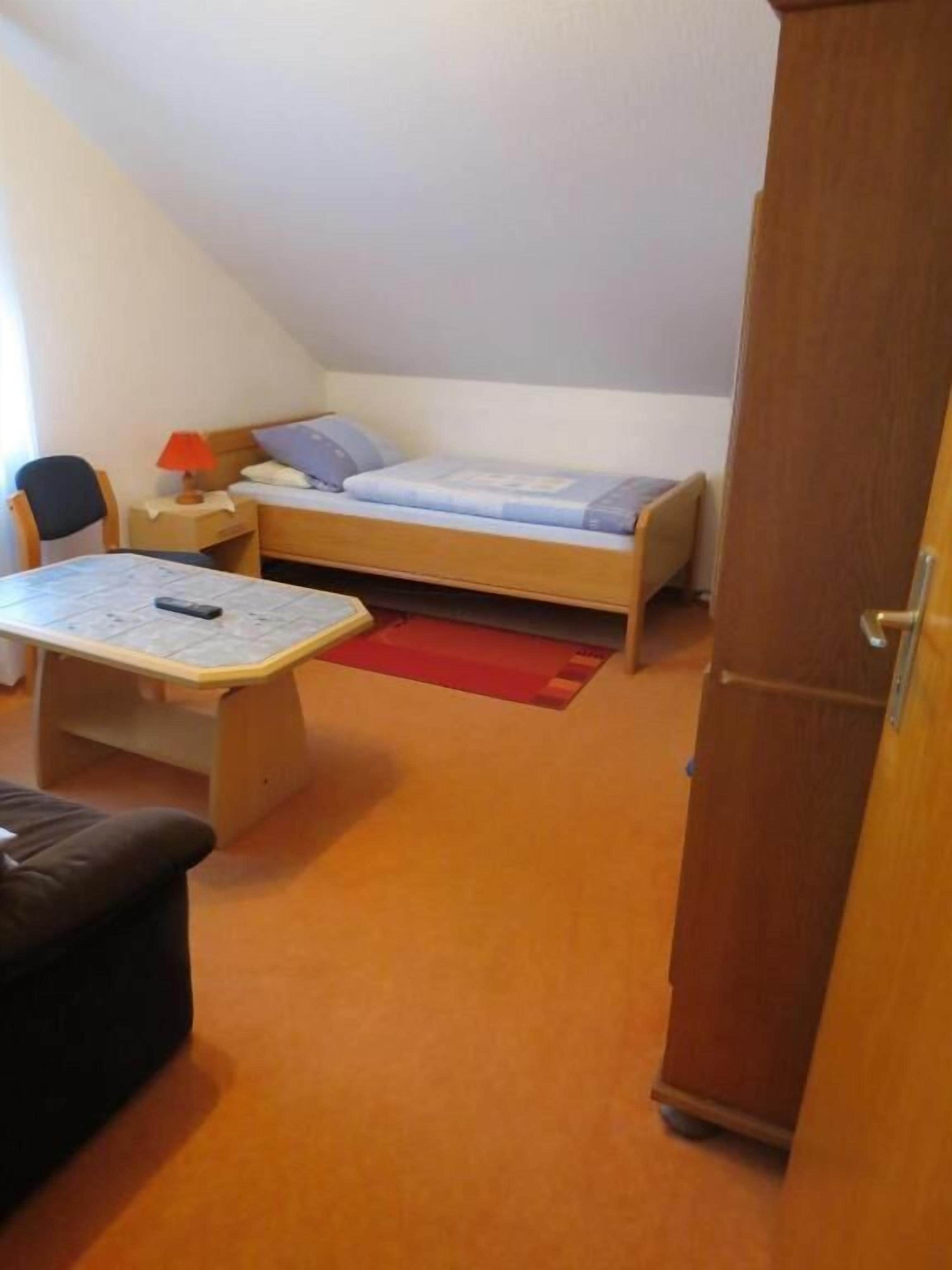 A small, single-room apartment with a bed, a desk, a chair, and a wardrobe.