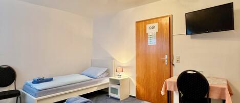 Quarto de hotel com cama, escrivaninha, cadeira, televisão e porta com placa.