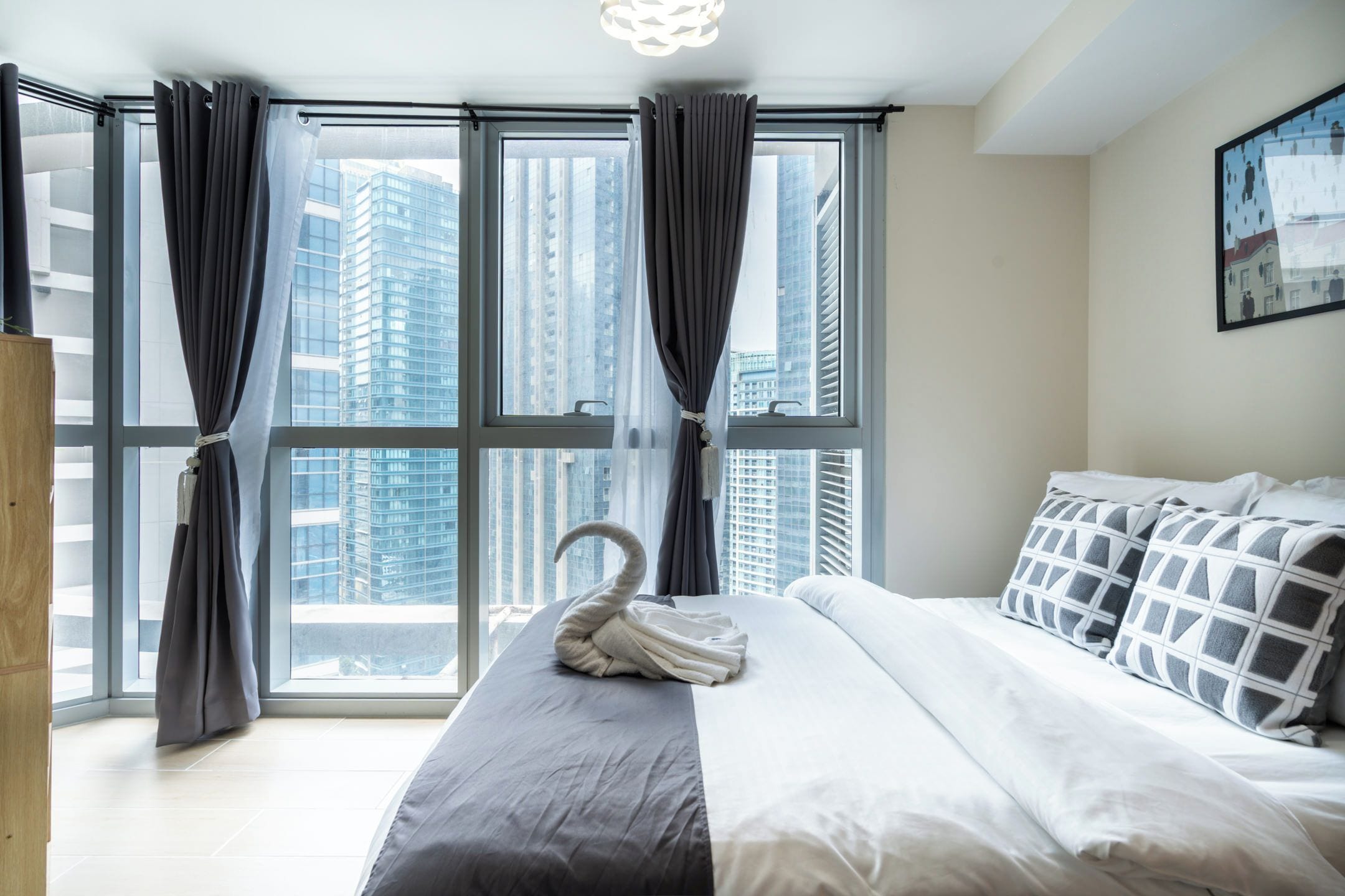 Ein modernes Hotelzimmer mit einem großen Bett, grau gestreuter Bettwäsche und einem schwanenförmig gefalteten Handtuch.