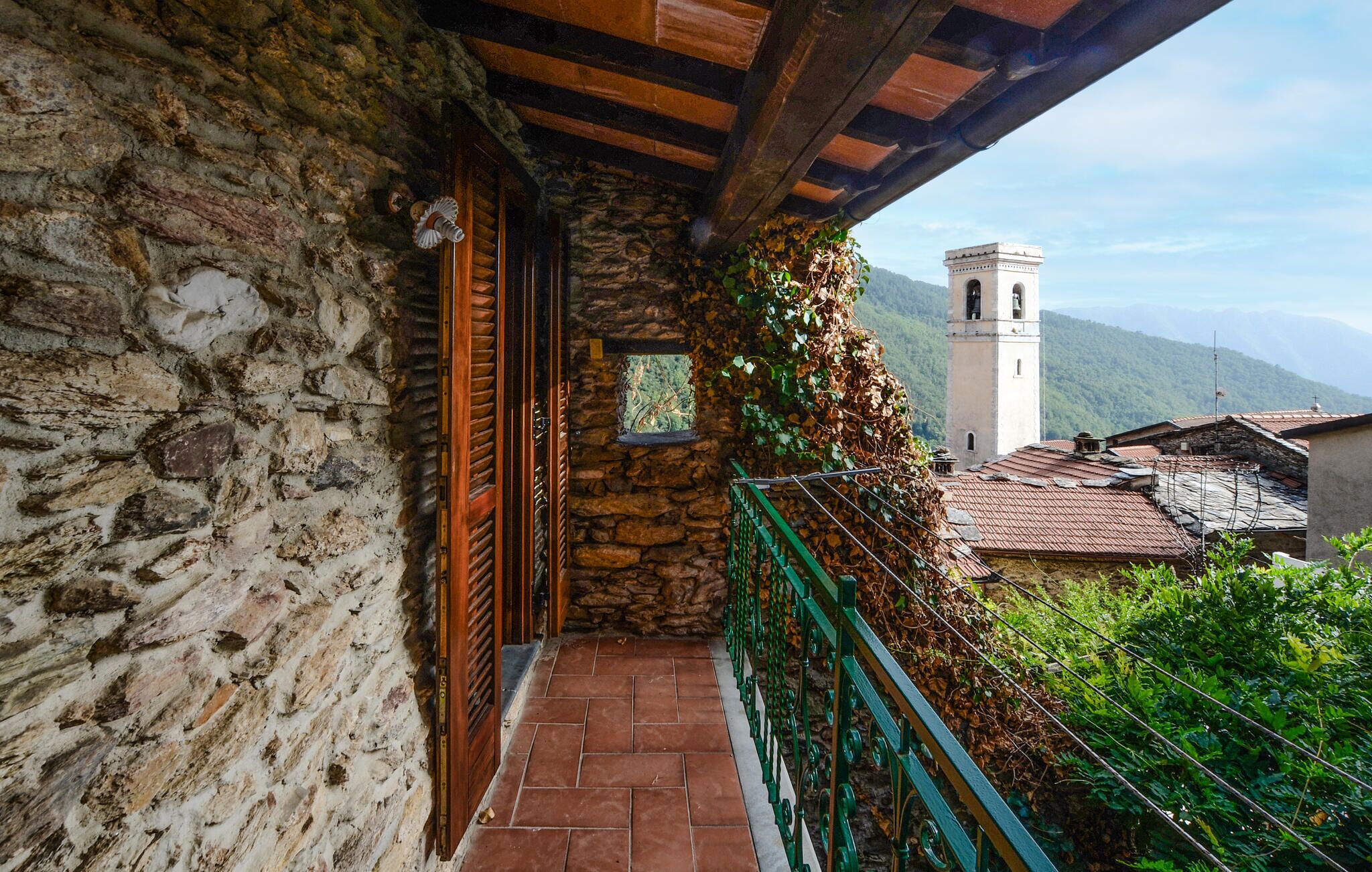 Un bâtiment en pierre avec une porte en bois et une fenêtre, un garde-corps en métal vert et une vue sur une tour au loin.