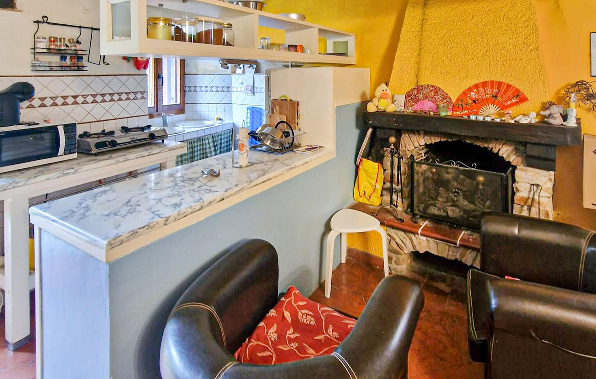 Een keuken met een marmeren aanrecht, een magnetron en een fornuis. Er is een open haard met decoratieve objecten erboven.