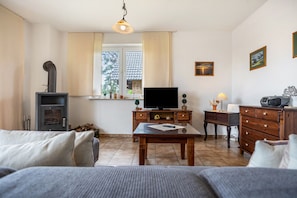 Ein Wohnzimmer mit einer Couch, einem Fernseher auf einem Holzschrank, einem Tisch mit einer Fernbedienung, einer Lampe und einem Kamin.