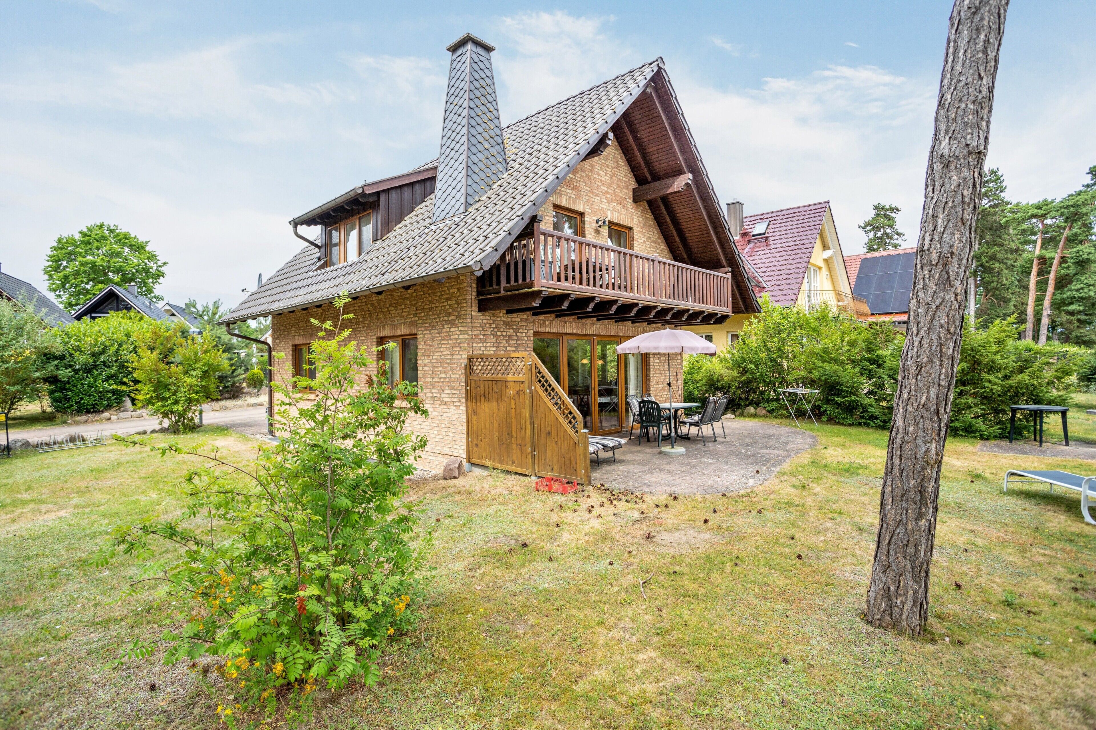 Ein zweistöckiges Haus mit einem Balkon, einer Terrasse mit Gartenmöbeln und einem Rasen.