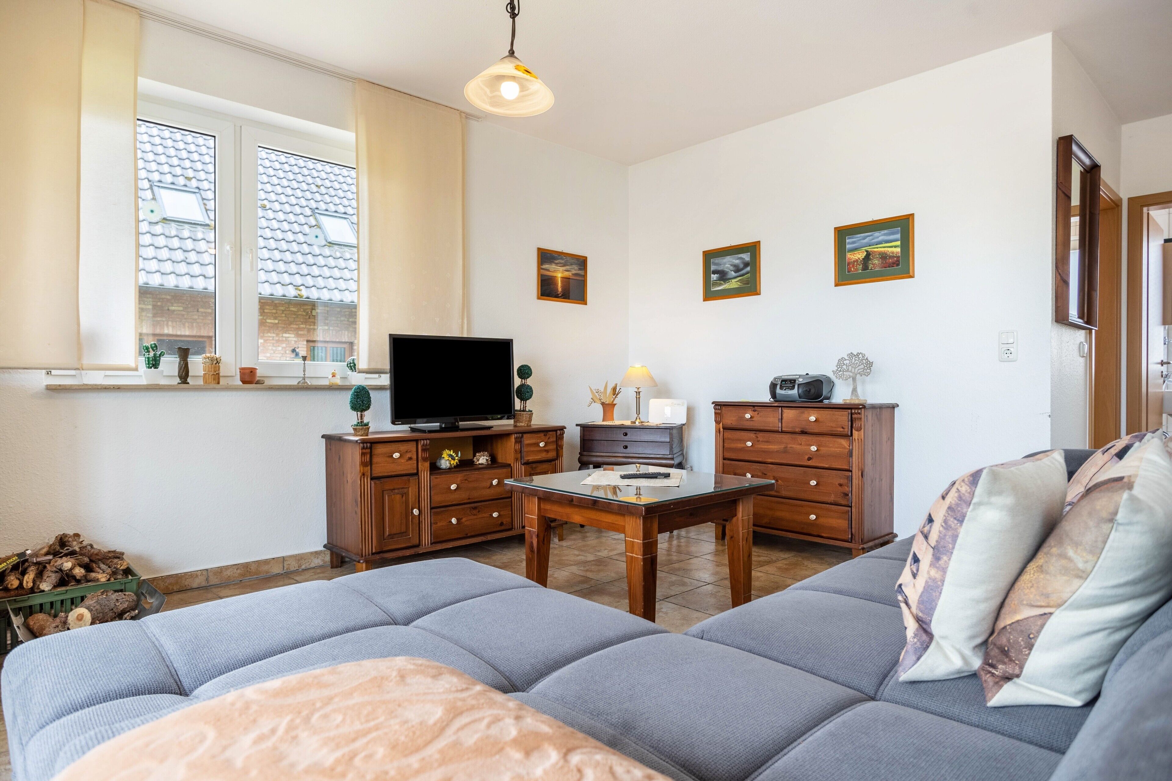 Ein Wohnzimmer mit einer Couch, einem Fernseher, Holzschränken und einem Fenster mit Blick auf ein Gebäude.