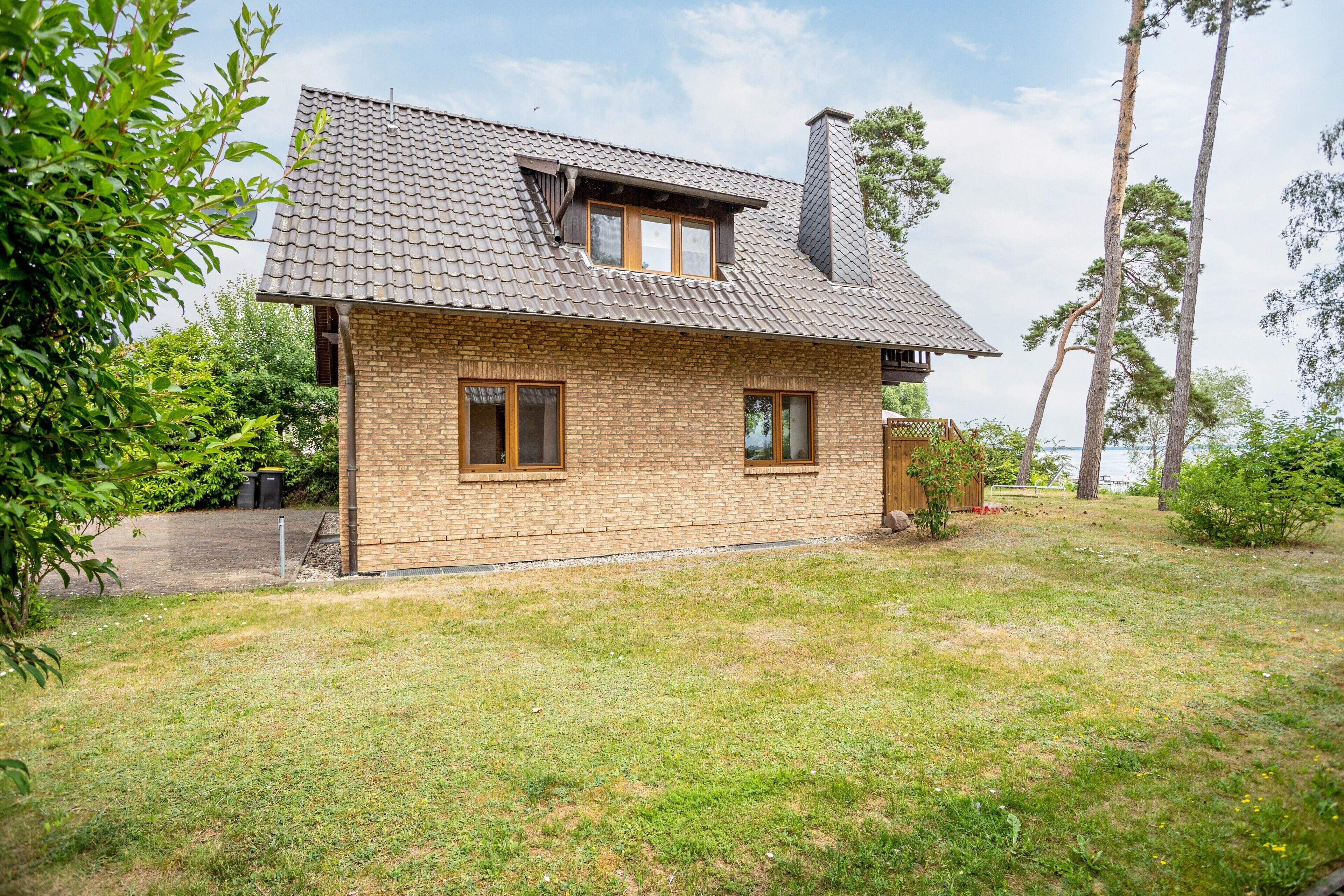 Ein zweigeschossiges Haus mit einem Ziegeldach und Backsteinwänden, umgeben von einem grasbewachsen Garten und Bäumen.
