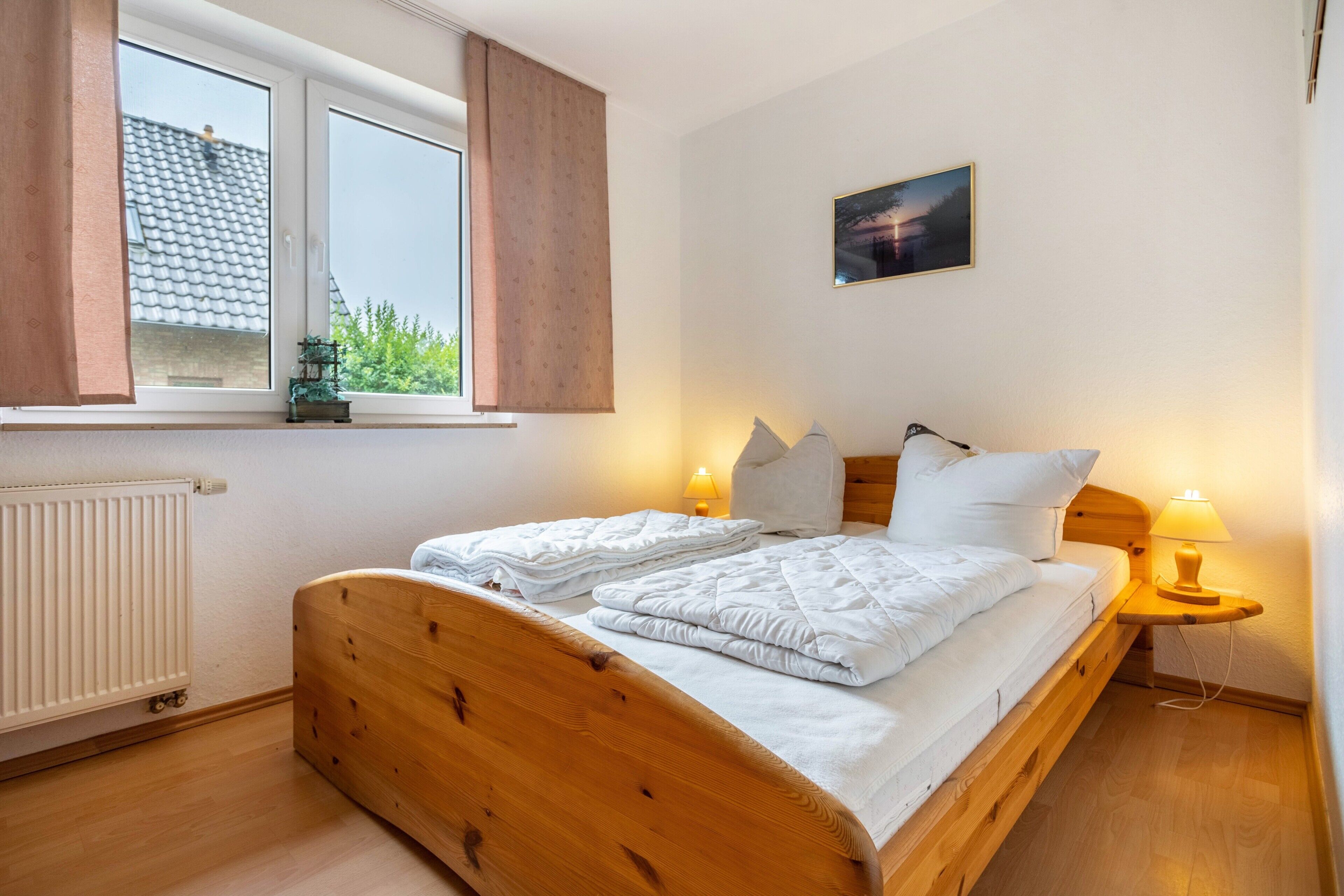 Ein ordentlich bezogenes Bett mit weißen Leinen, einem Holz-Kopfteil und einem Fenster mit Vorhängen.