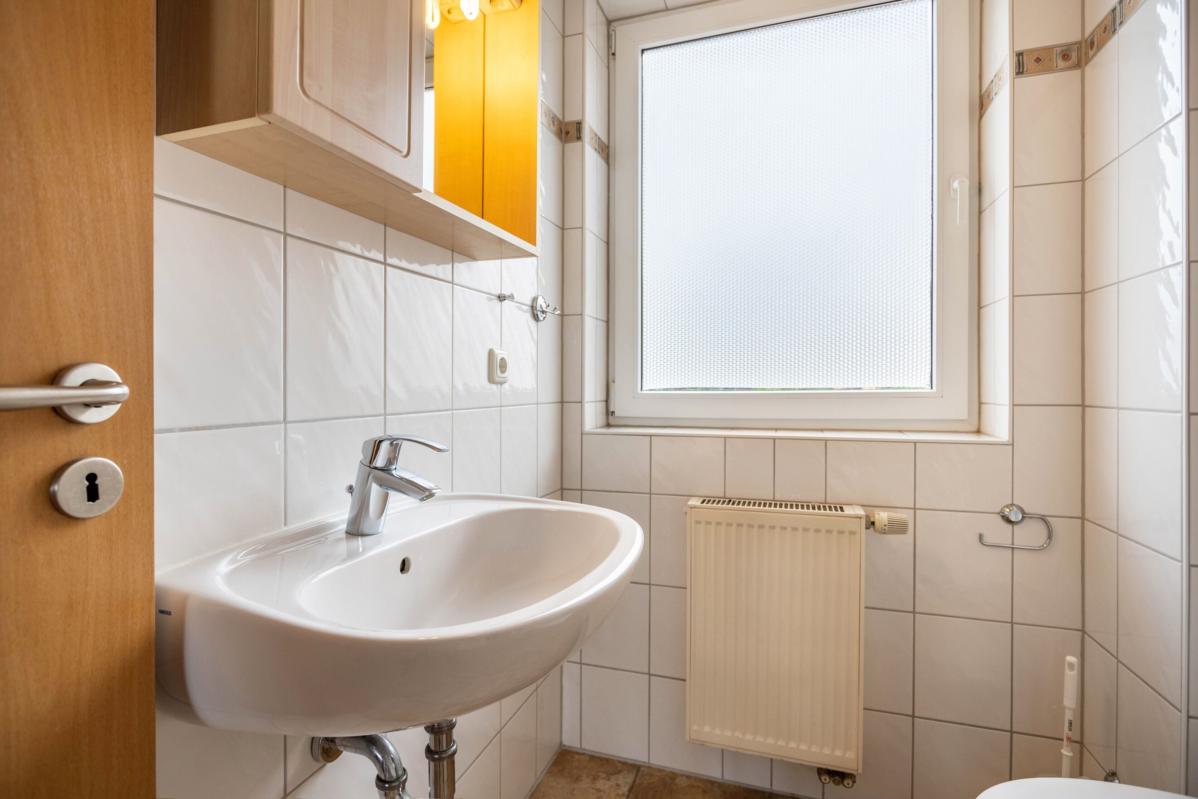 A bathroom with a white sink, a mirror above it, a window, and a radiator.